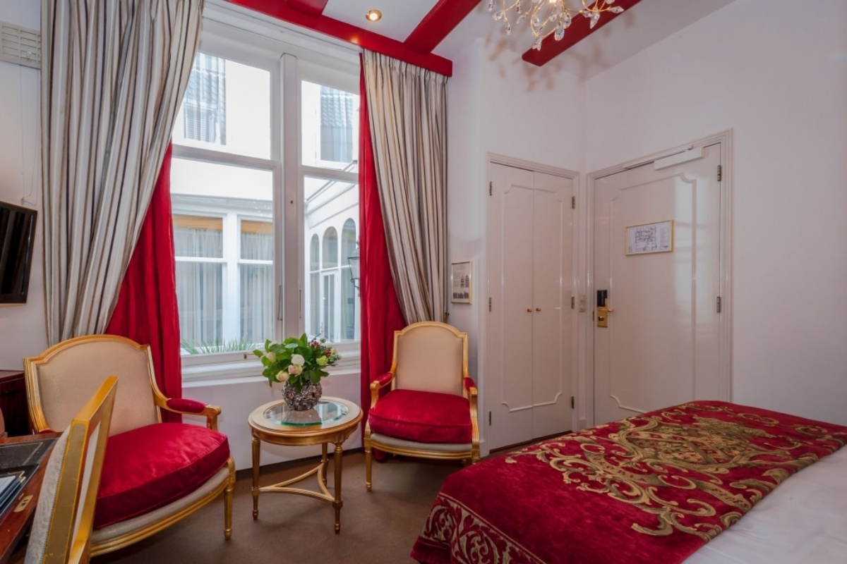 Ambassade Hotel - a room with red curtains and a bed and chairs