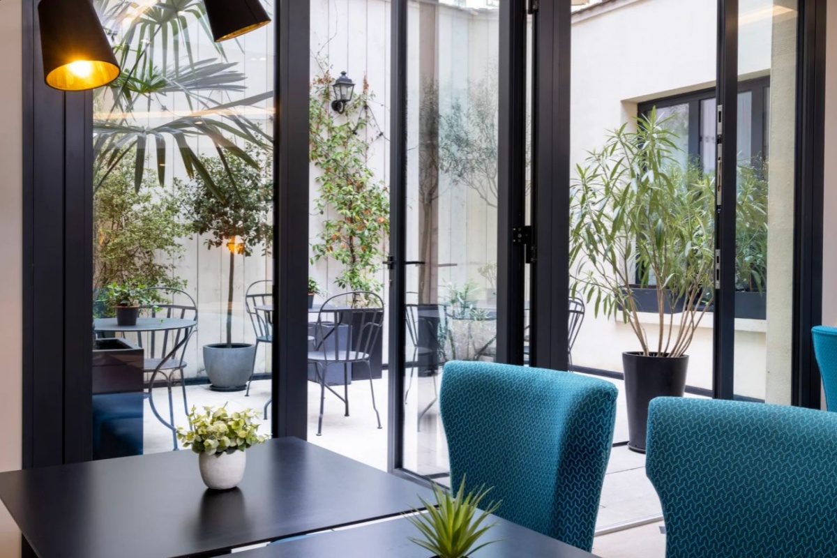 Hotel Gustave - a table with chairs and plants in front of a glass door