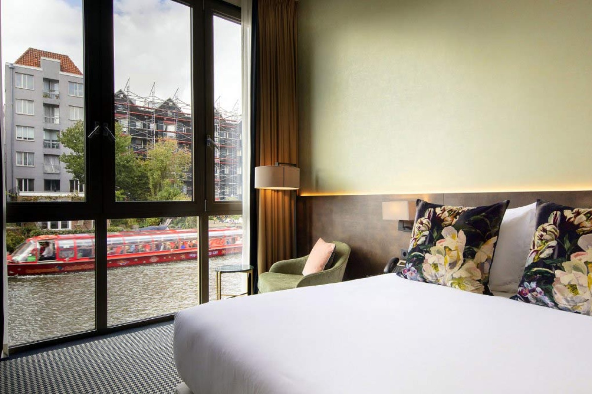 Monet Garden Hotel Amsterdam - a bed with a flowered pillow and chair in a room with a river