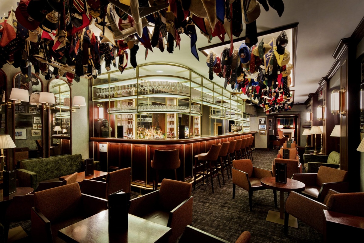 The Stafford London - a room with a bar and chairs and a table with hats from the ceiling