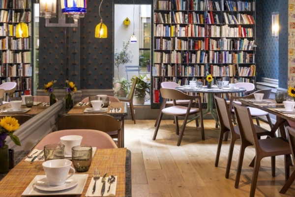 Hotel de Londres Eiffel - a room with a book shelf and tables and chairs