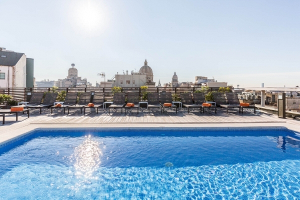 Hotel Jazz - a pool with chairs and a building in the background