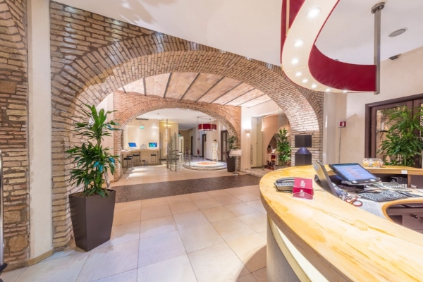 Kolbe Hotel Rome - Hotel reception area with a tiled floor, brick walls with arch detail and potted plants. 