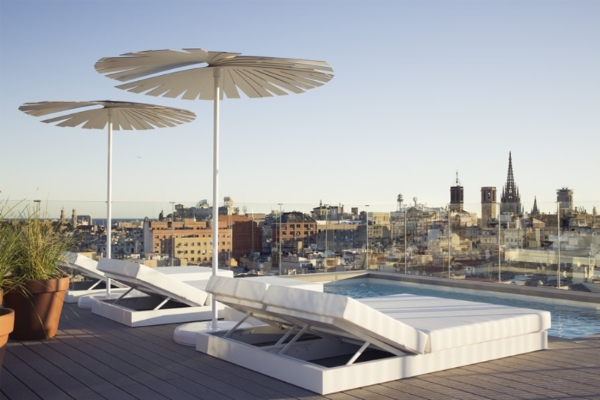 Yurbban Trafalgar Hotel - a pool with umbrellas and a deck with a city in the background